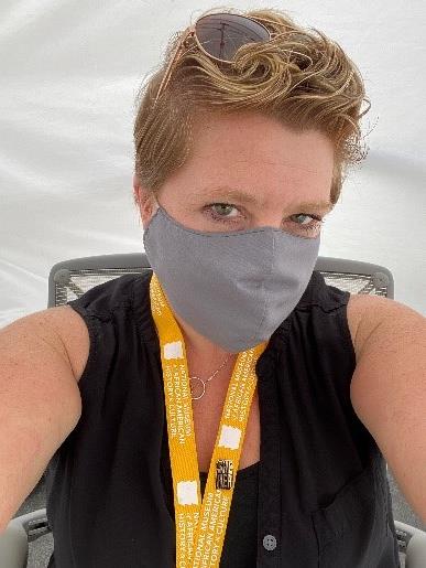 In her headshot, Tammy has her short, dark blonde hair parted on one side. She is wearing a black shirt and vest, gray face mask and yellow lanyard.